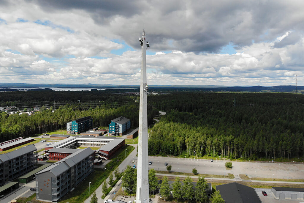 Hantverkare syns på en hög spira. De genomför underhållsarbete och målar spiran.